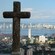 A Christian cross overlooks a sprawling city by a bay